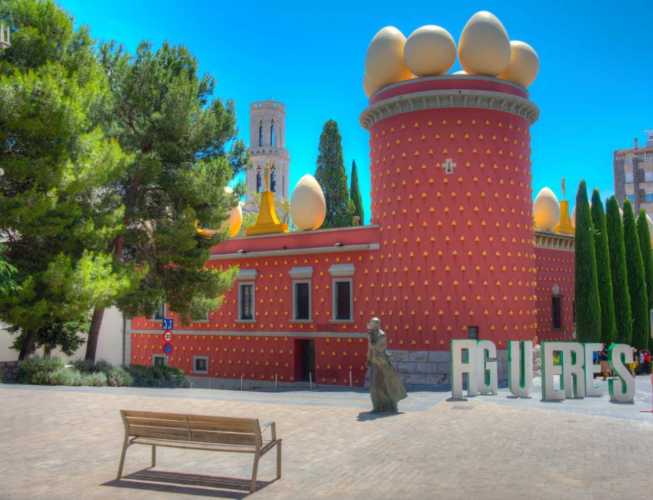 Il Teatro-Museo Dalí di Figueres con un albero sulla sinistra, una statua di fronte e un cielo azzurro sullo sfondo.