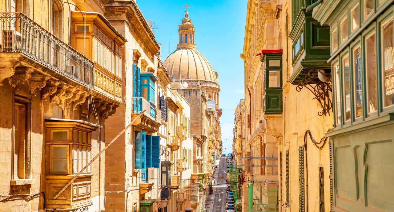 A steep uphill street surrounded by old yellow stone buildings and a church at the bottom with a large dome.