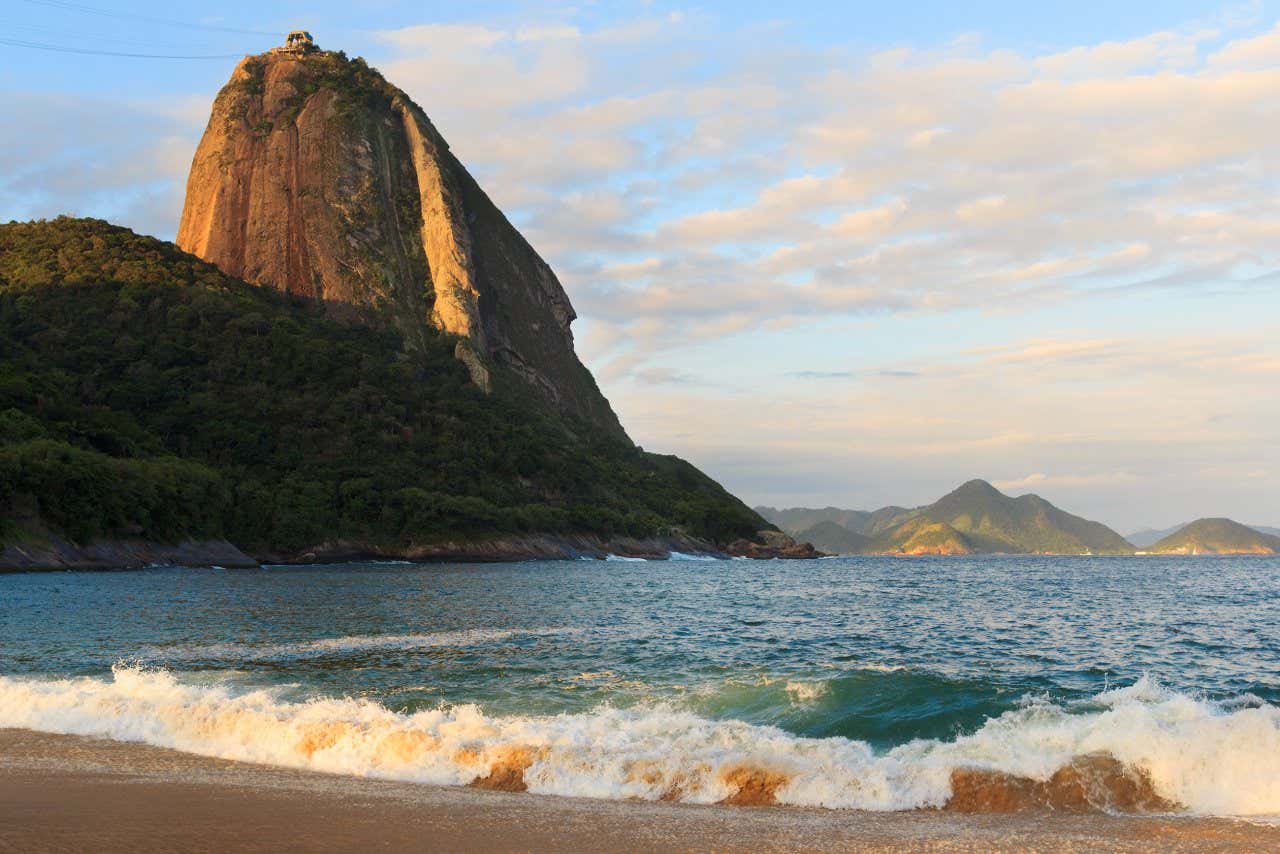 Onde quebrando na areia avermelhada da praia Vermelha com o Pão de Açúcar ao fundo ao entardecer