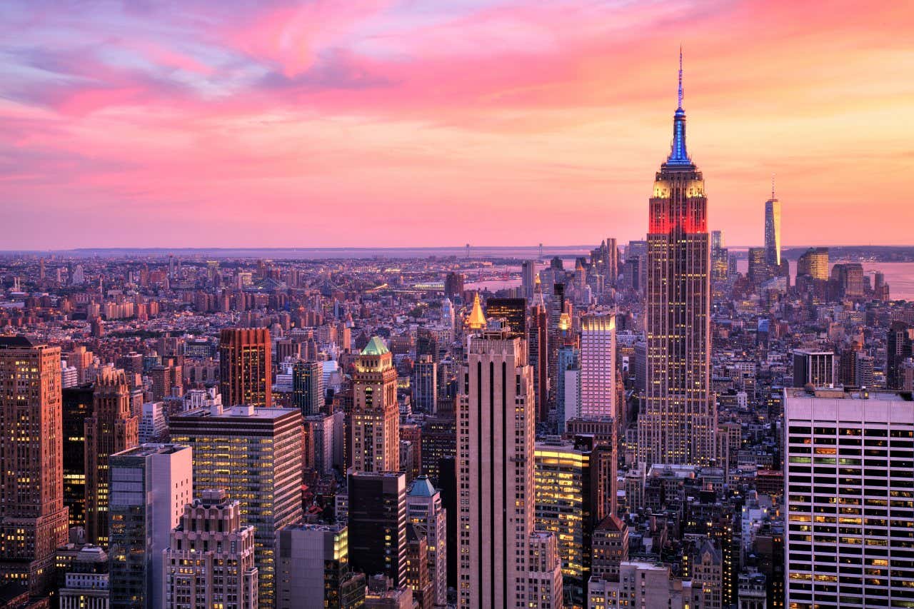 The city of New York at dusk with an orange and pink sunset.