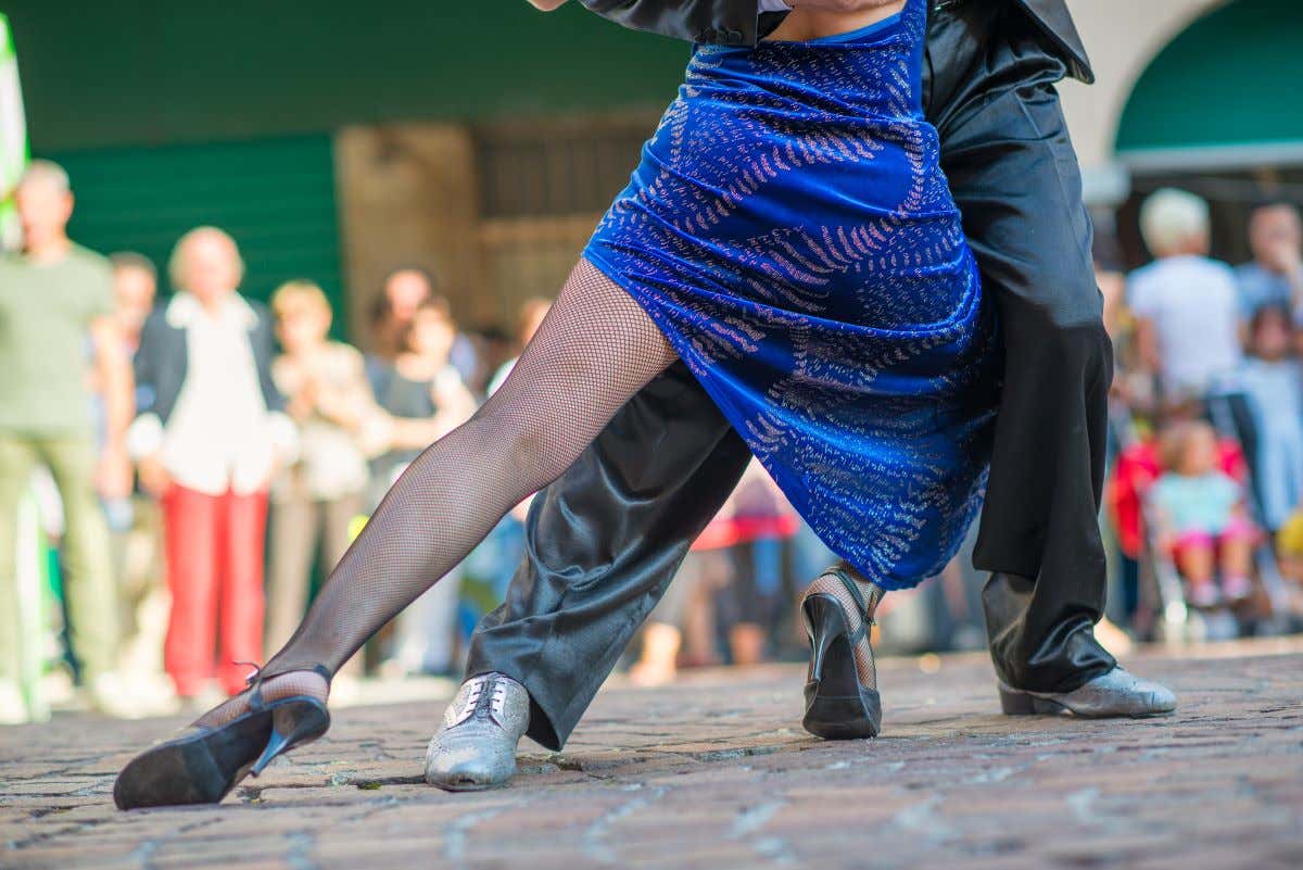 Una pareja bailando tango en una calle mientras un grupo de gente los mira