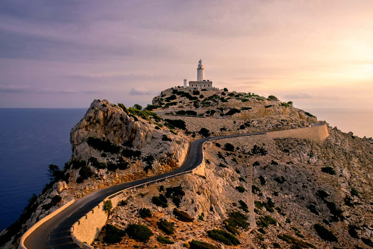 El cielo se tiñe de colores sonrosados al atardecer frente al faro del cabo de Formentor, ubicado en una colina en primera línea del mar