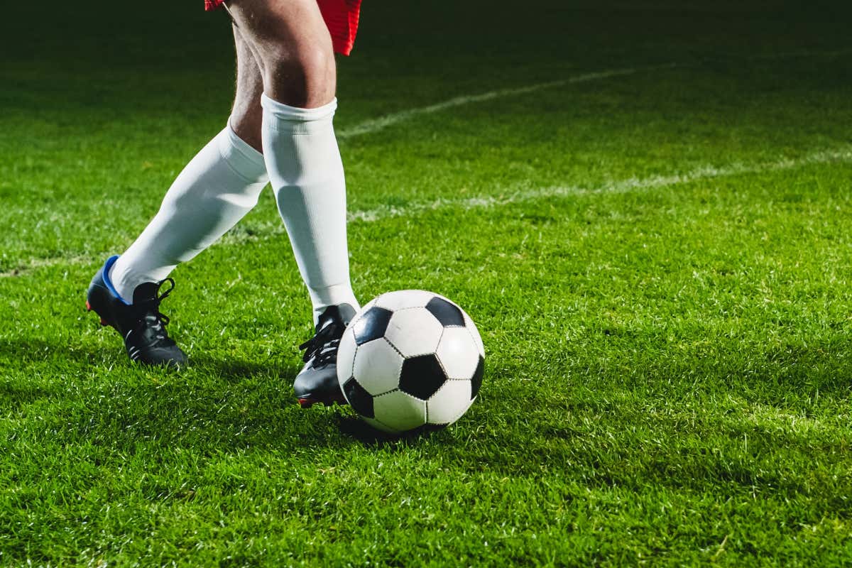 Plan rapproché sur les jambes d'un footballeur avec un ballon à ses pieds sur un terrain