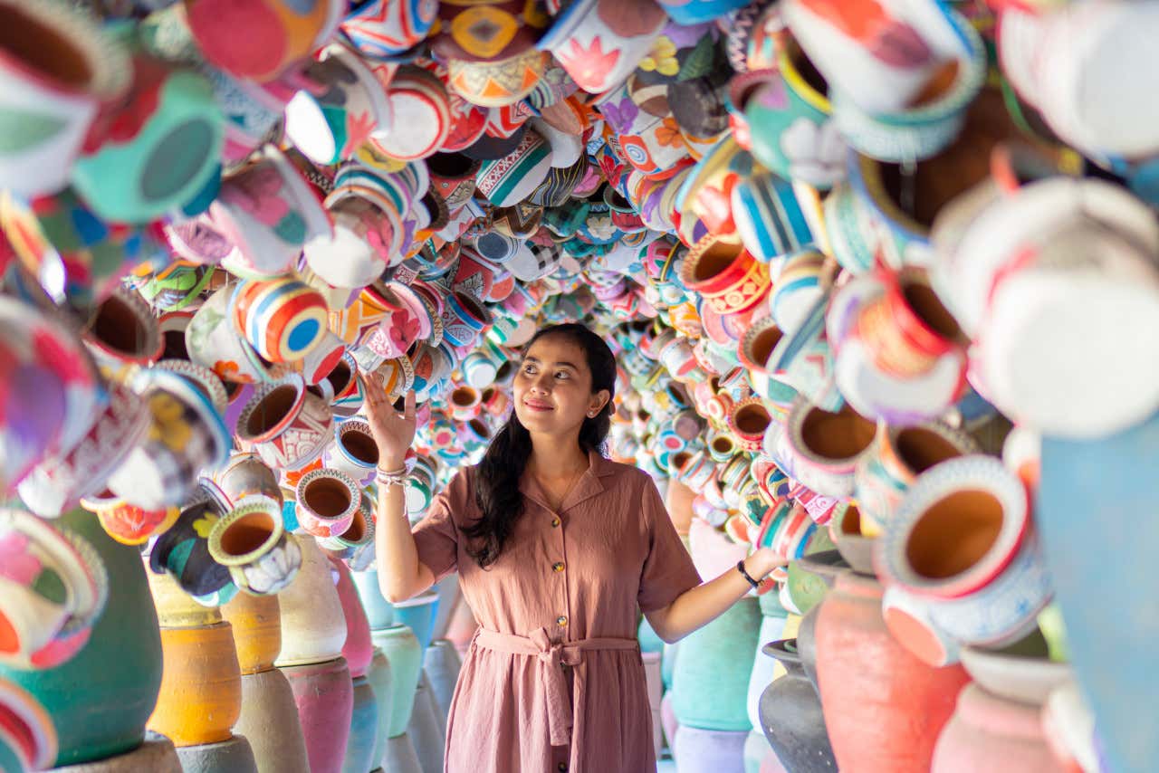 Una mujer pasando por un pasillo con tazas de cerámicas colgadas a los laterales