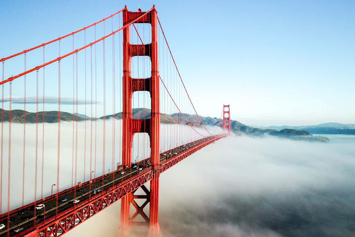 Panoramic view of the red Golden Gate Bridge crossed by several cars in heavy fog.