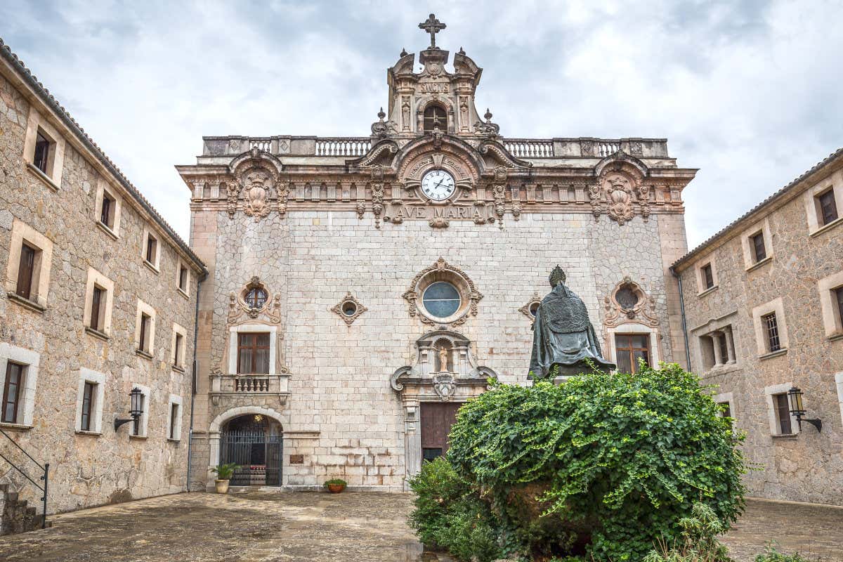 Santuario de Lluc con una fachada de piedra donde destaca un reloj y unas letras de Ave María y con una escultura de bronce al frente