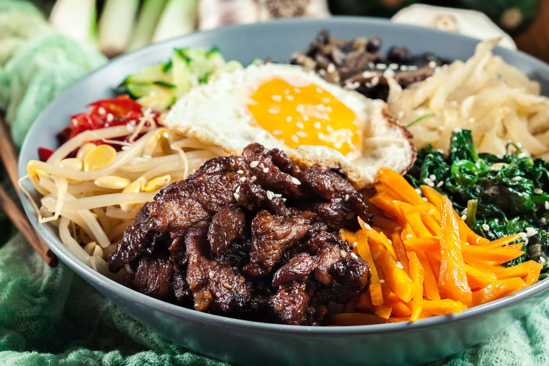 Una ciotola di bibimbap, con un uovo, germogli, verdure e carne visibili.