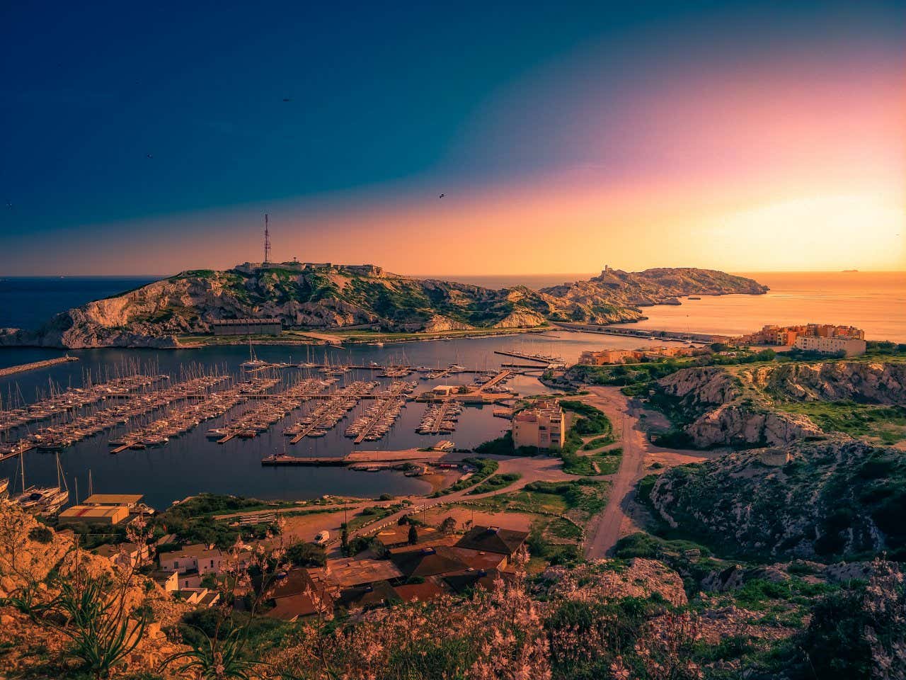 The island Ratonneau and a small port with surrounding paths and vegetation as the sun sets