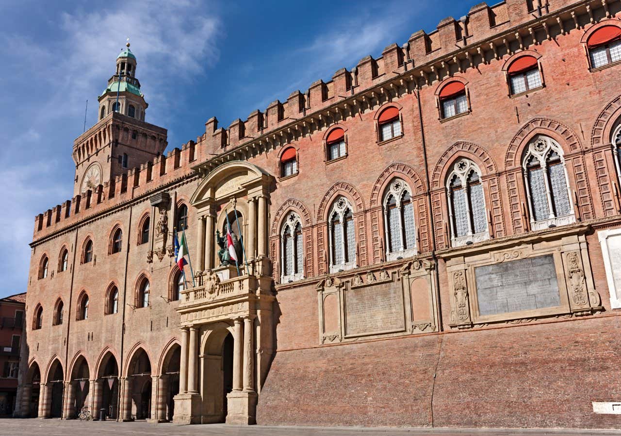 Un grosso palazzo di mattoni con le bandiere istituzionali, finestre con archi gotici, sormontato dalla torre dell'orologio