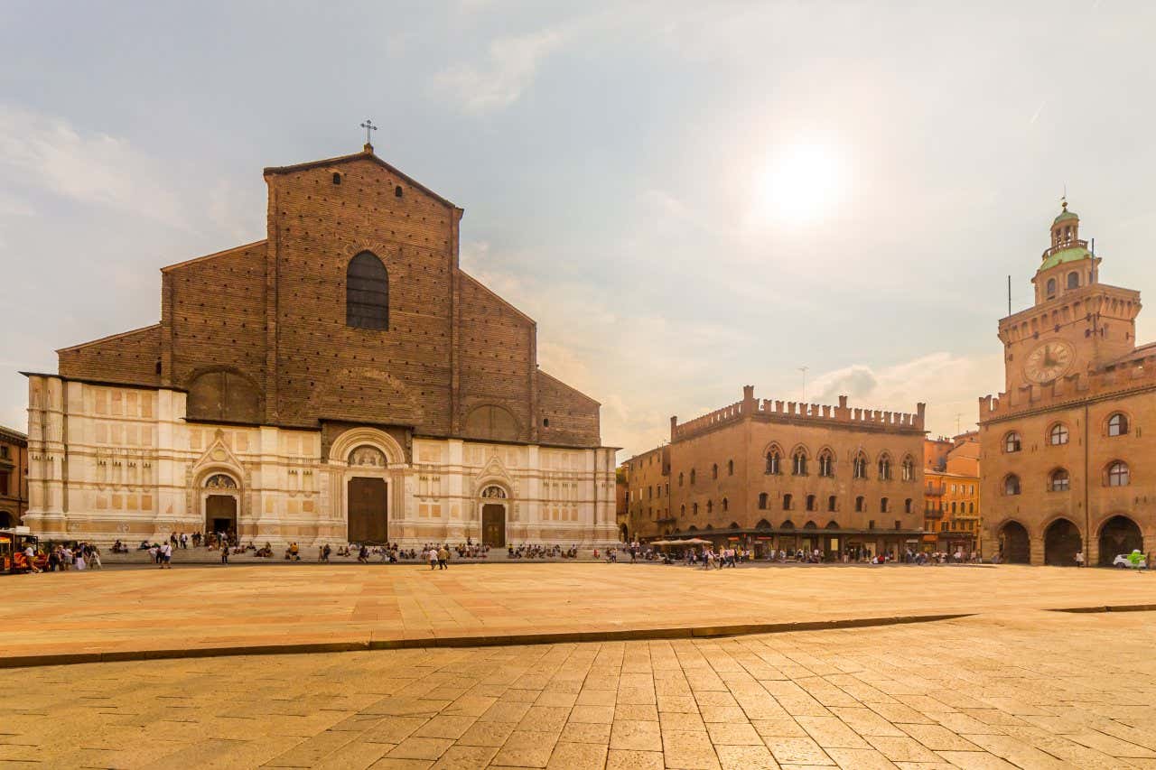 La grande Piazza Maggiore con la facciata dell'enorme Basilica di San Petronio, ricoperta di marmo solo per metà, e alcune persone sedute sui suoi scalini