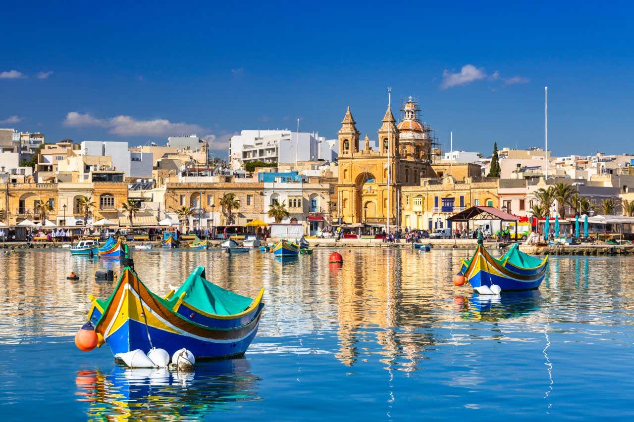 Plusieurs bateaux colorés dans l'eau avec la ville en fond sous un ciel bleu