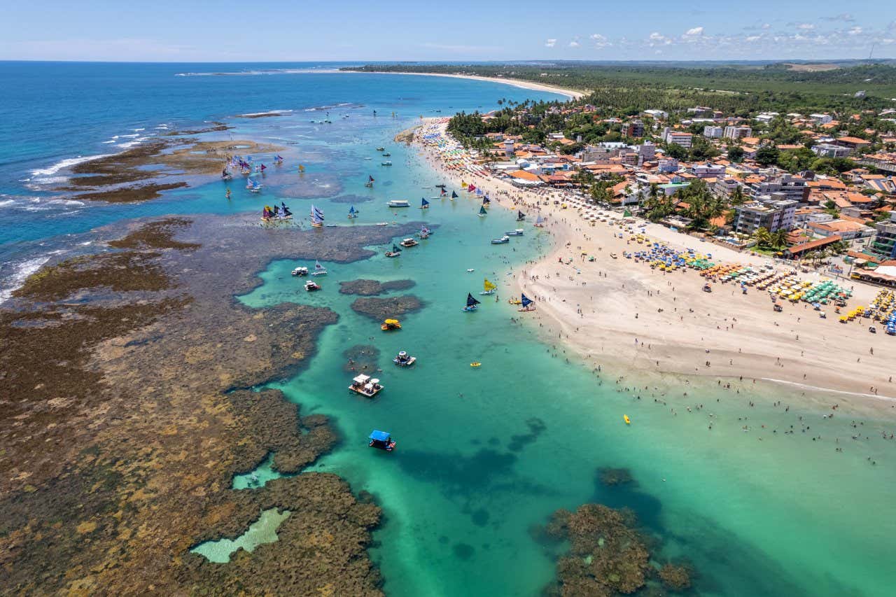 Vue panoramique sur la plage de Porto de Galinhas avec de nombreux bateaux et des parasols colorés et les bâtiments de la ville à l'arrière-plan