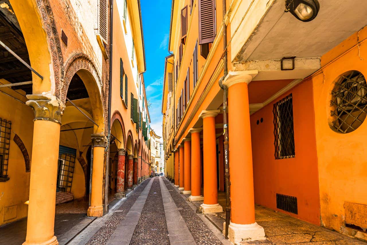 Una stretta via del centro di Bologna con i portici caratteristici e i tipici palazzi storici di colore rosso arancione