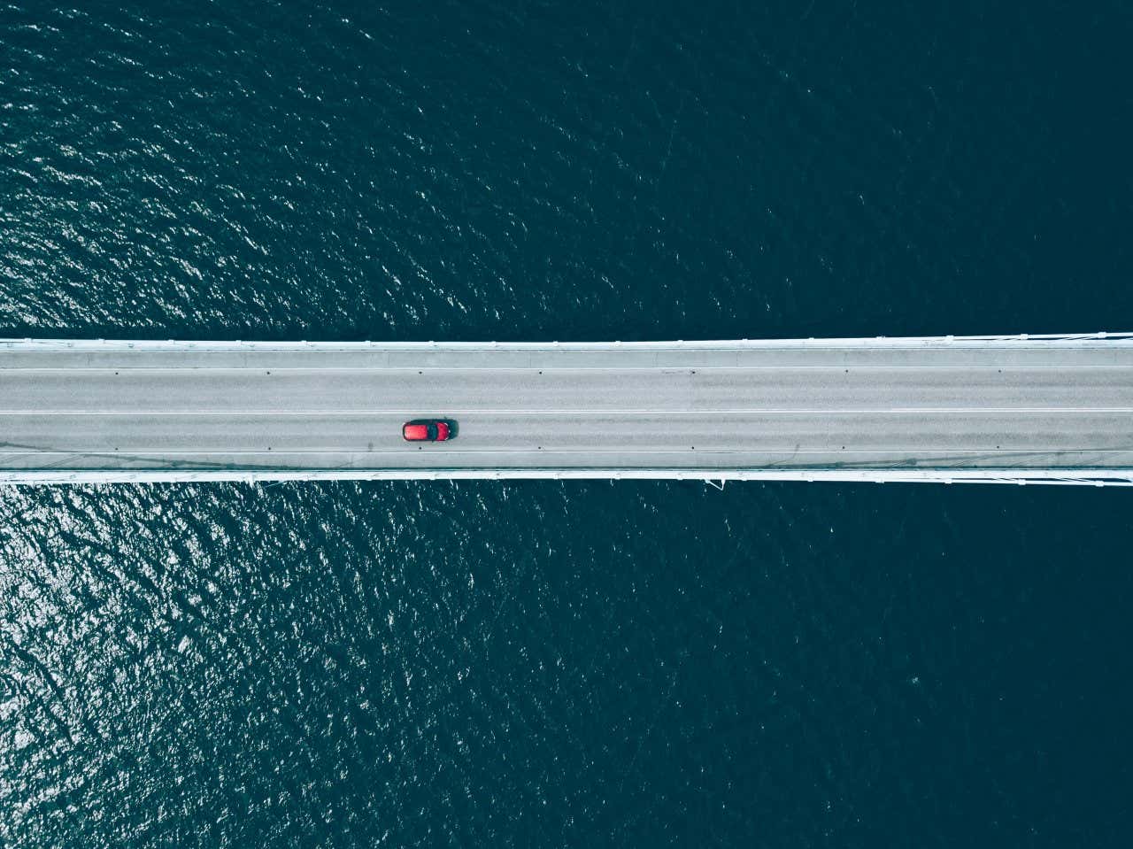 Vista dall'alto di una macchina rossa che attraversa un ponte in cemento sopra una distesa d'acqua