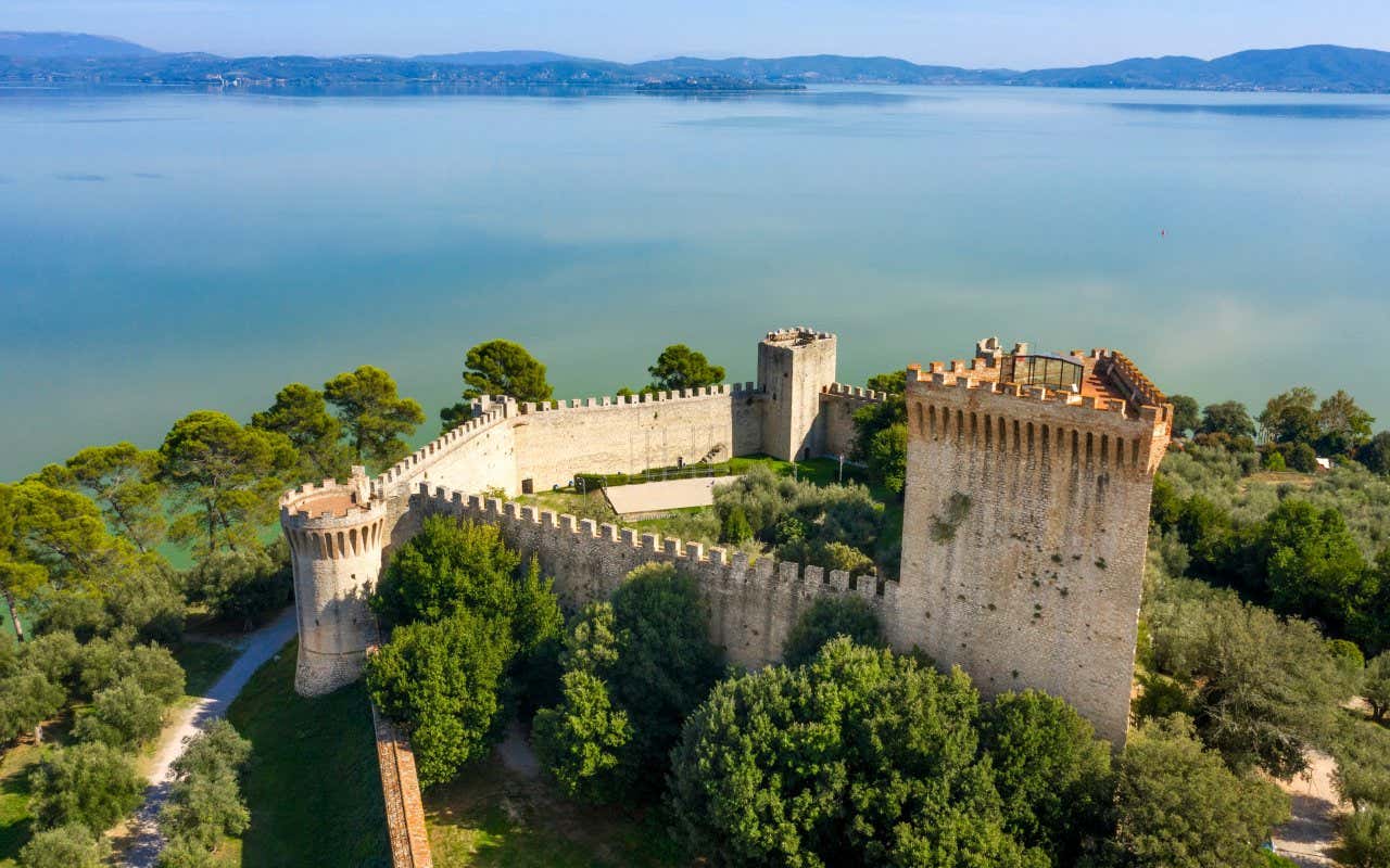 Una piccola fortezza in pietra bianca vista dall'alto con davanti un grande lago d'acqua turchese in un giorno di sole