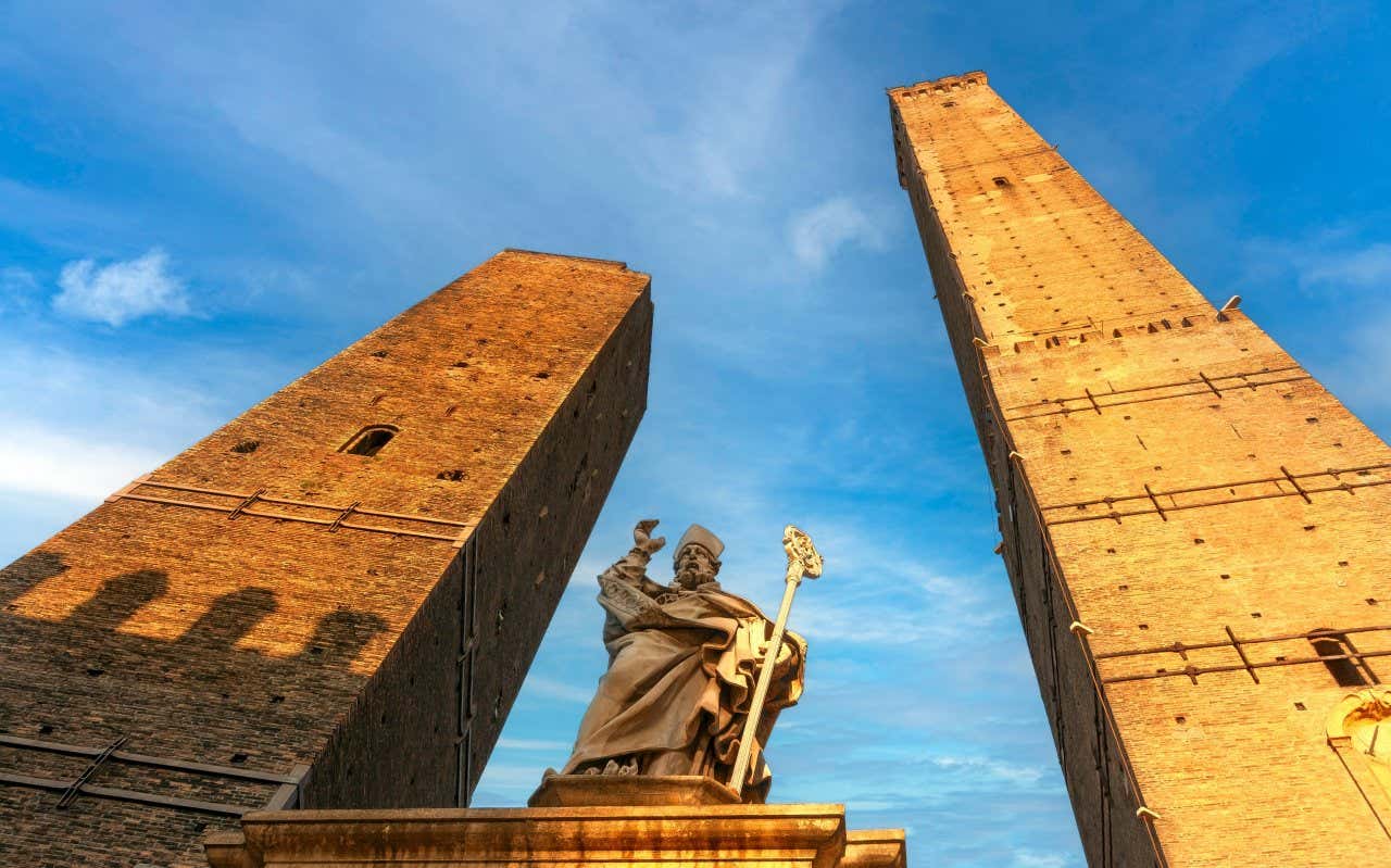 Le due torri Garisenda e degli Asinelli riprese dal basso con in mezzo la statua di un vescovo. La torre degli Asinelli, a destra, è nettamente più alta dell'altra