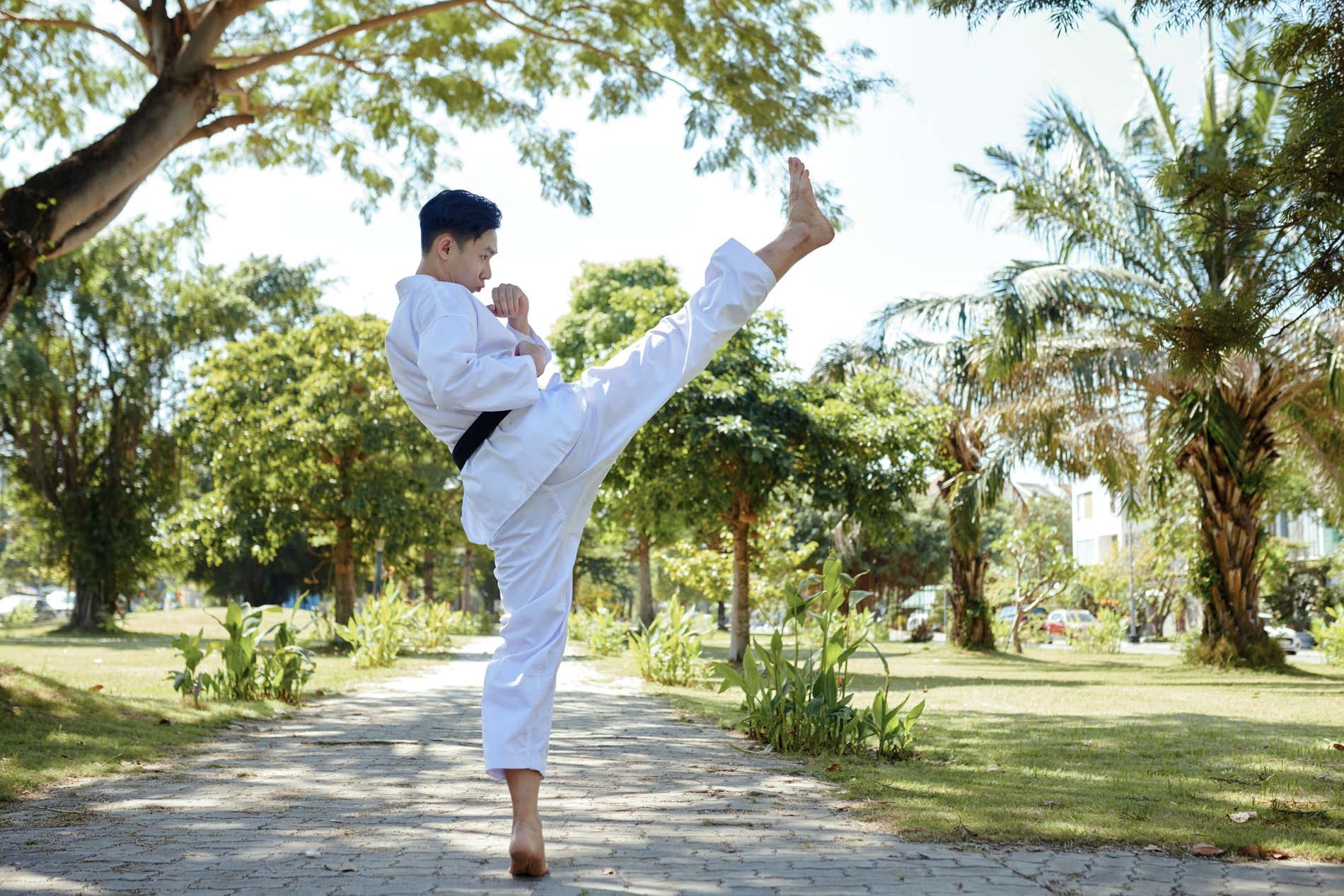 Un uomo sul sentiero di un parco, praticando un calcio dell'arte marziale Taekwondo