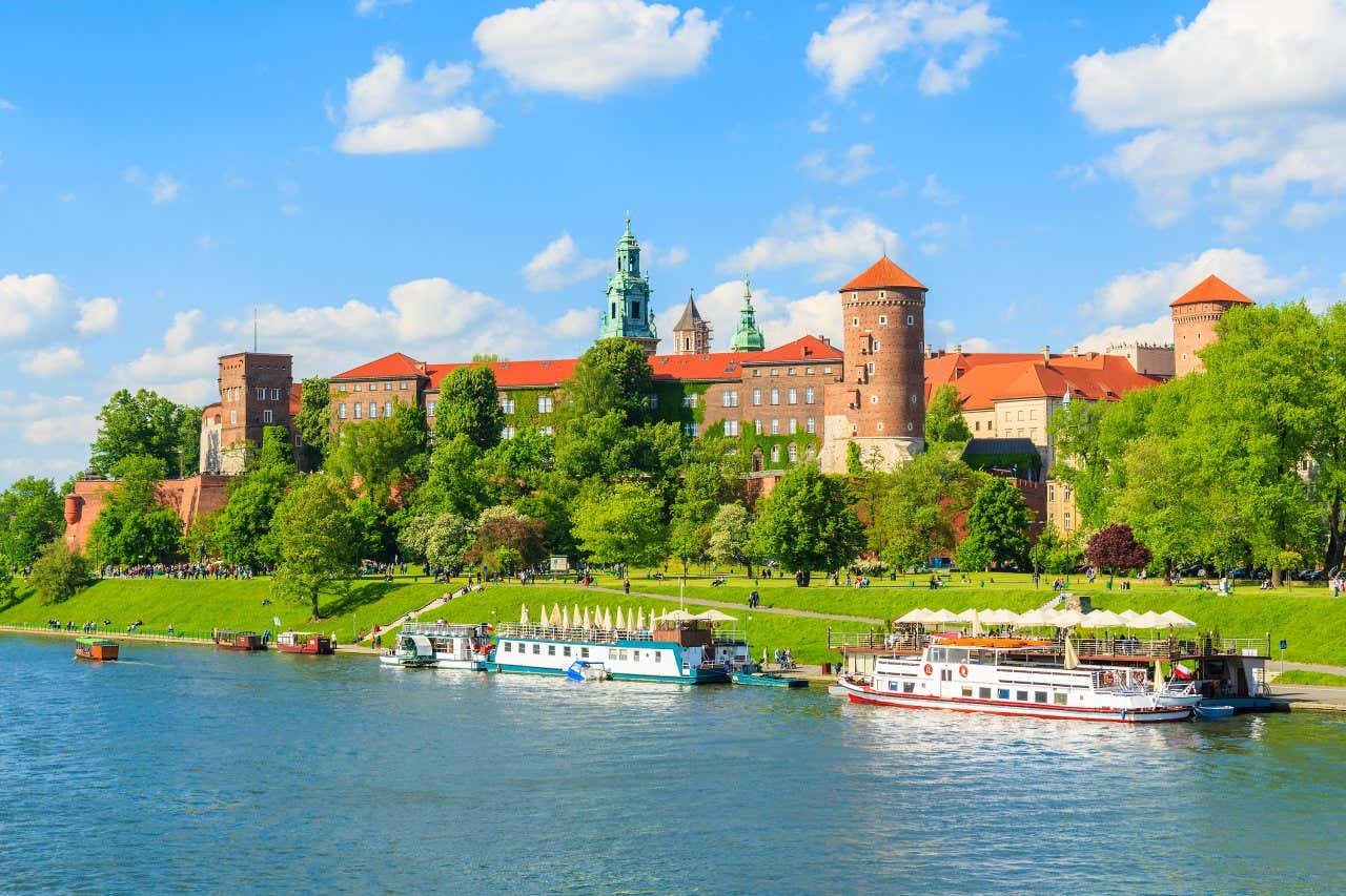 2 boats on the Vistula River with Wawel Castle and a cloudy blue sky in the background.