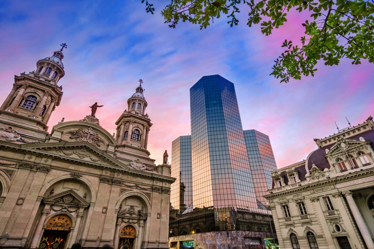 Façade de la cathédrale de Santiago avec un gratte-ciel en fond au coucher du soleil, l'un des lieux à visiter à Santiago du Chili