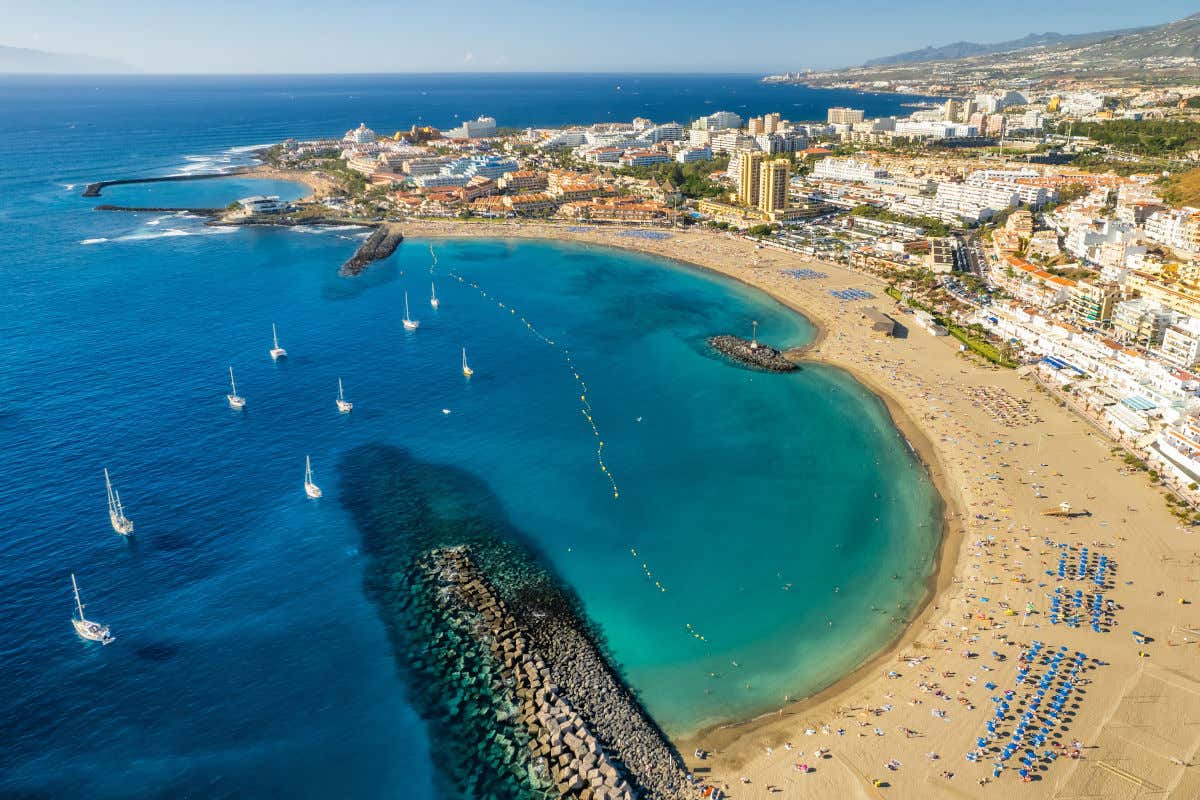 Aerial view of Las Vistas beach, a bay of golden sand and deep blue waters surrounded by hotel and residential buildings in Tenerife.