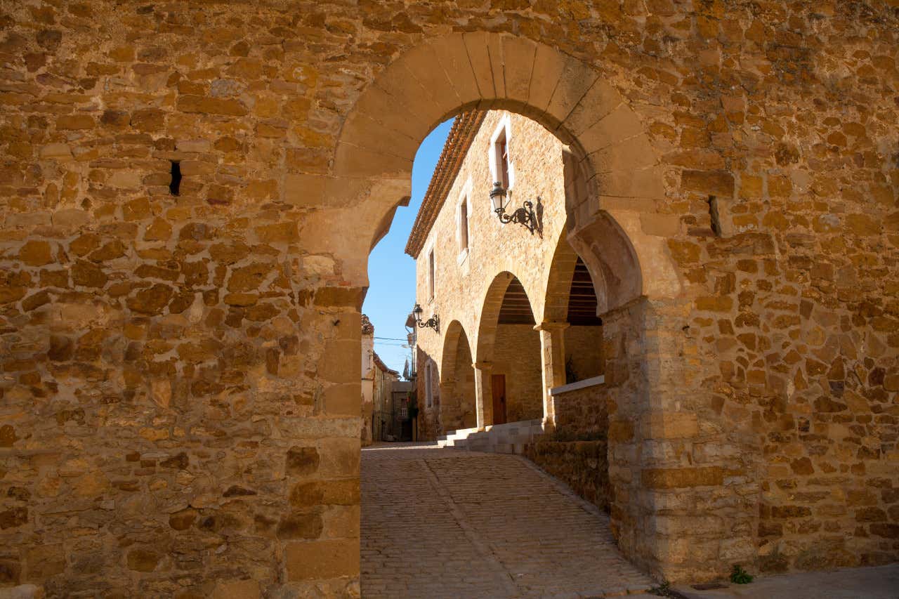 Un arco en Benasal a través del cual se ve una calle porticada y el cielo azul