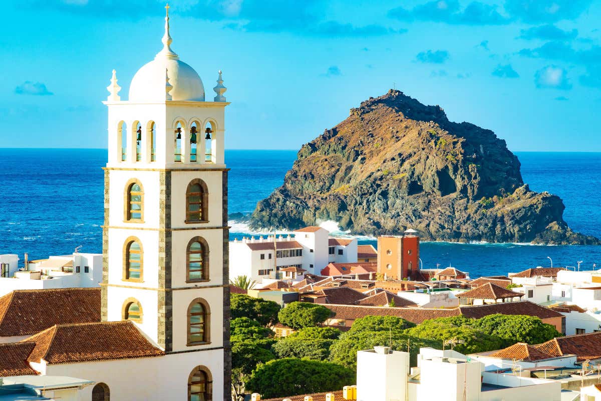 A gigantic volcanic rock in the middle of the sea in front of houses and a church.