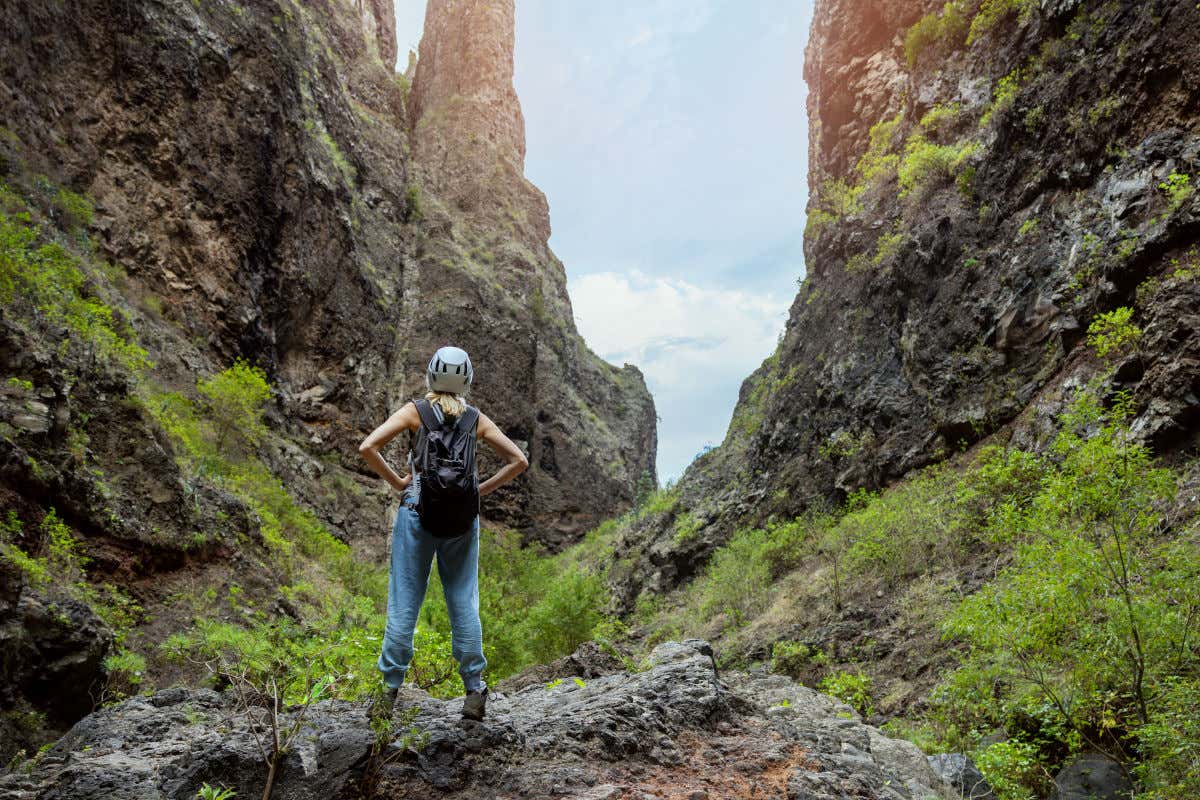 A woman wearing a helmet with her back to the camera while hiking in Tenerife in a steep-walled ravine.