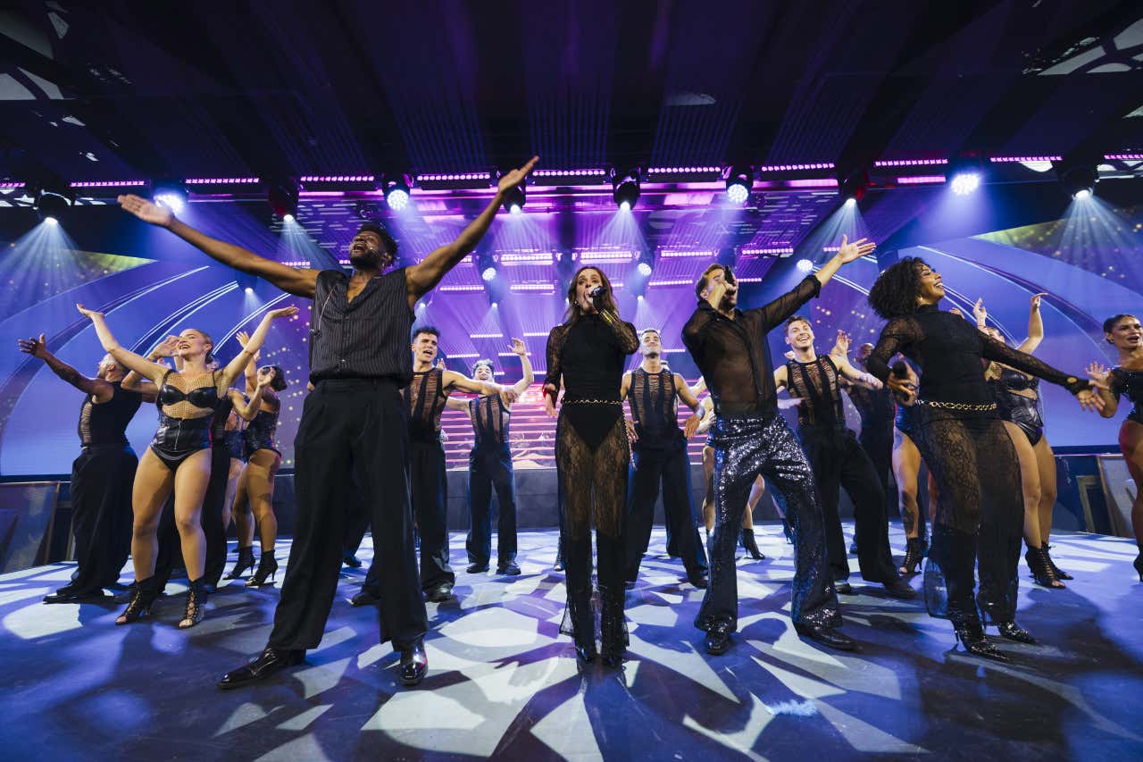 Un grupo de cantantes y bailarines vestidos de negro en mitad de un escenario