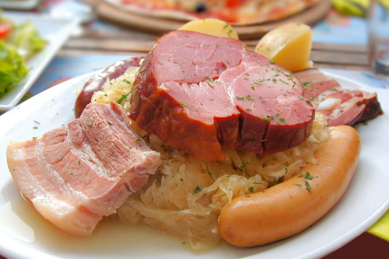 Un plat de Choucroute avec différents types de viande, du chou cuit et de la pomme de terre, goûter aux spécialités et une activité que vous devez faire en Alsace