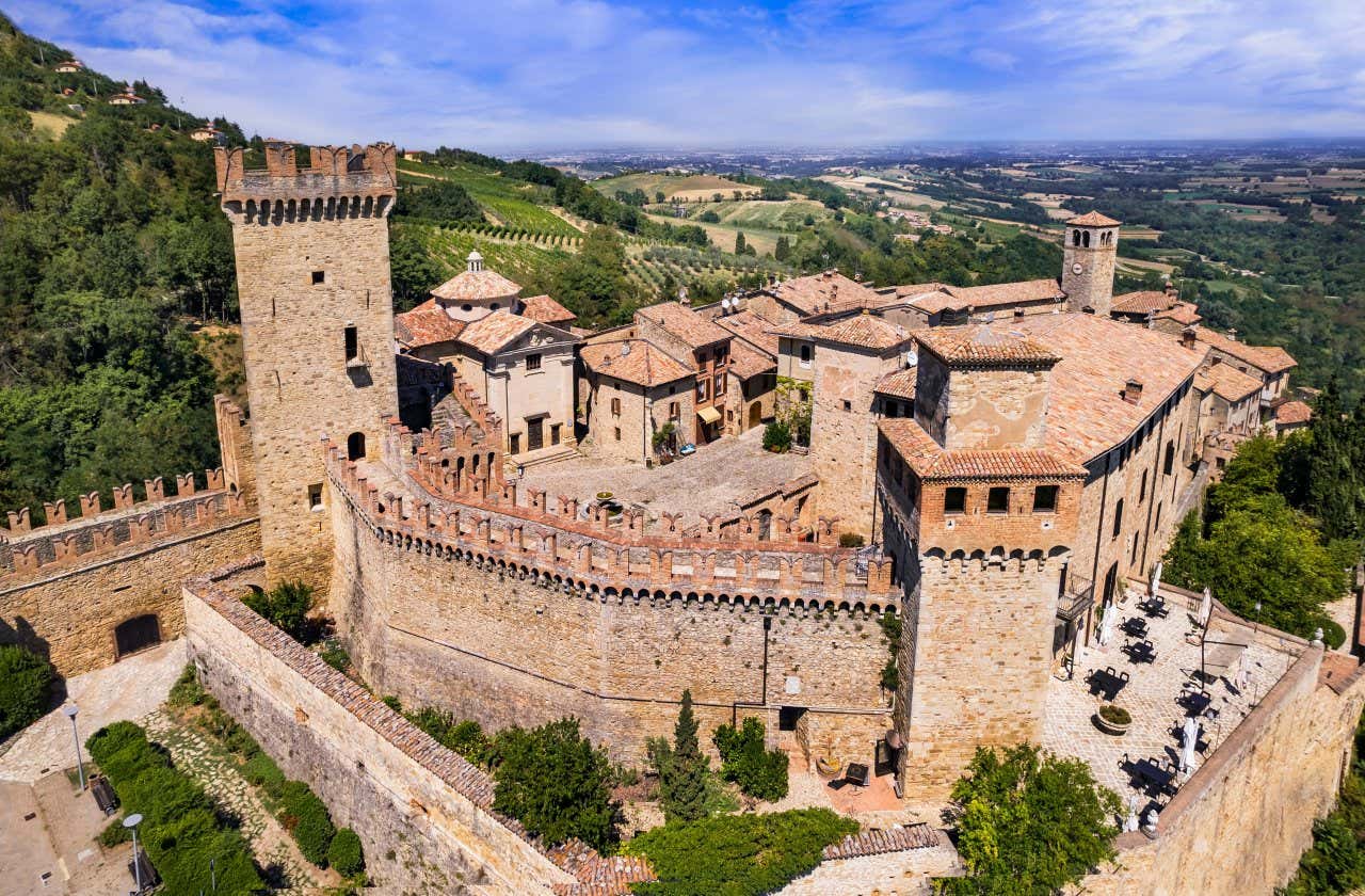 Vista dall'alto di un borgo in pietra in cima a un monte alberato, con mura di cinta con torri e piccole case in pietra all'interno del perimetro fortificato