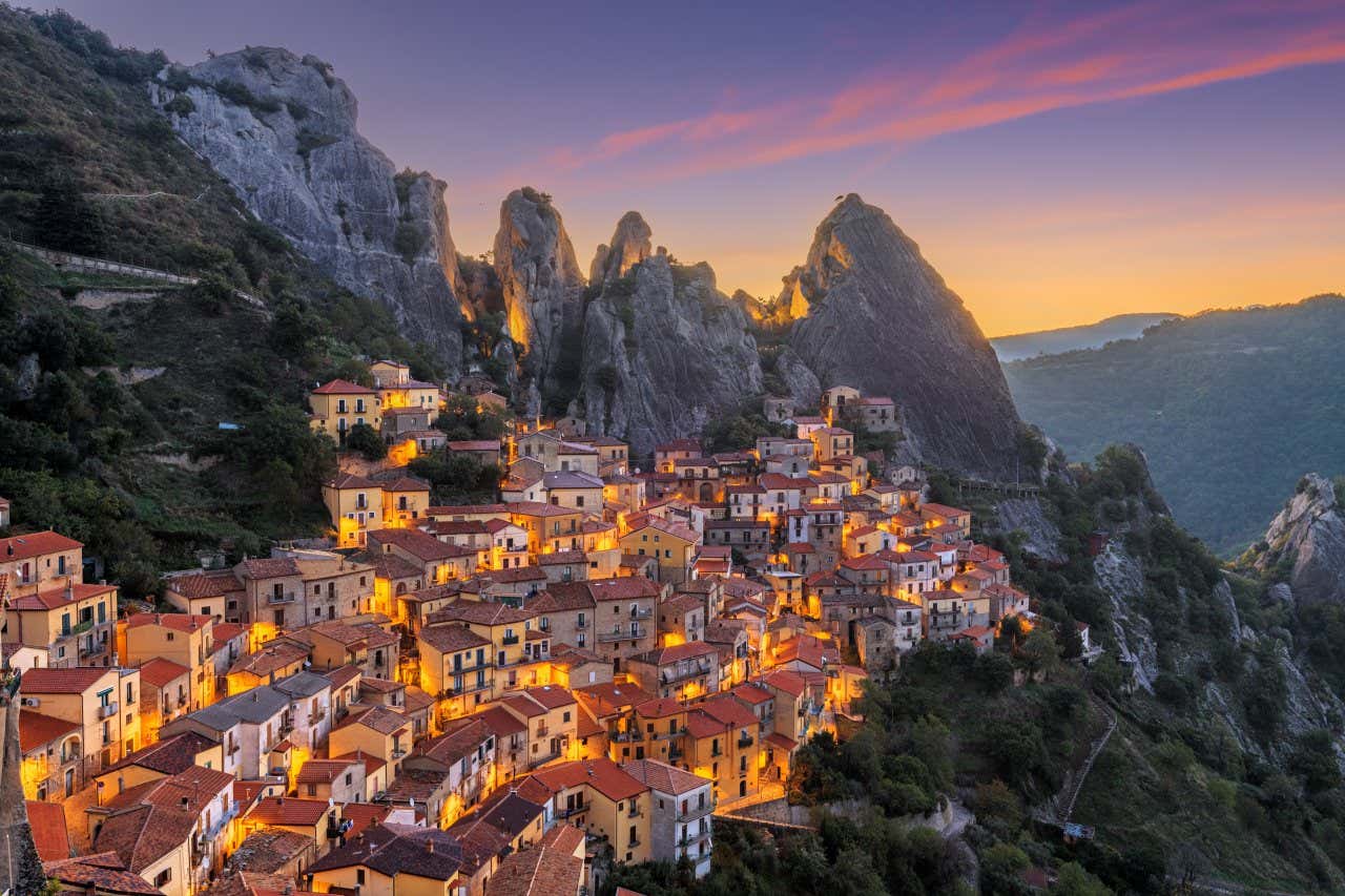 Un piccolo villaggio costruito sulla cima di una montagna ripreso dall'alto al tramonto illuminato da luci notturne arancioni