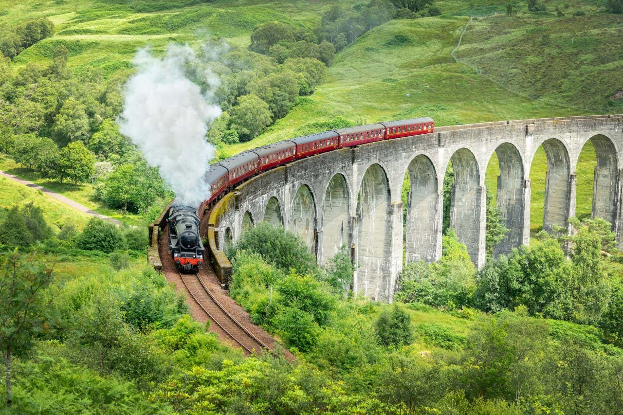 Vista aérea do trem Jacobite passando pelo Viaduto Glenfinnan rodeado de vegetação