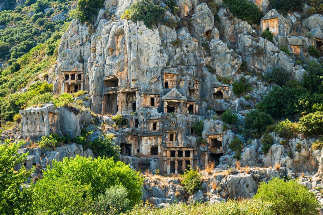 Buildings carved into a mountain in Demre, Turkey with vegetation all around it.