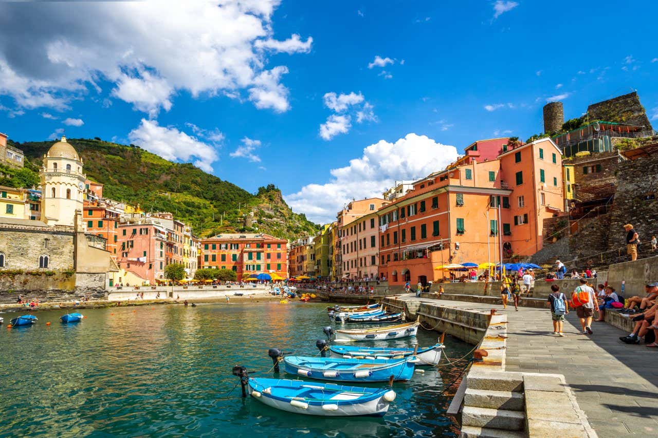 Vernazza vista dal porto, con alcune barchette in legno in primo piano sul mare e piccoli edifici colorati in arancione e giallo arroccati sulle colline rocciose circostanti