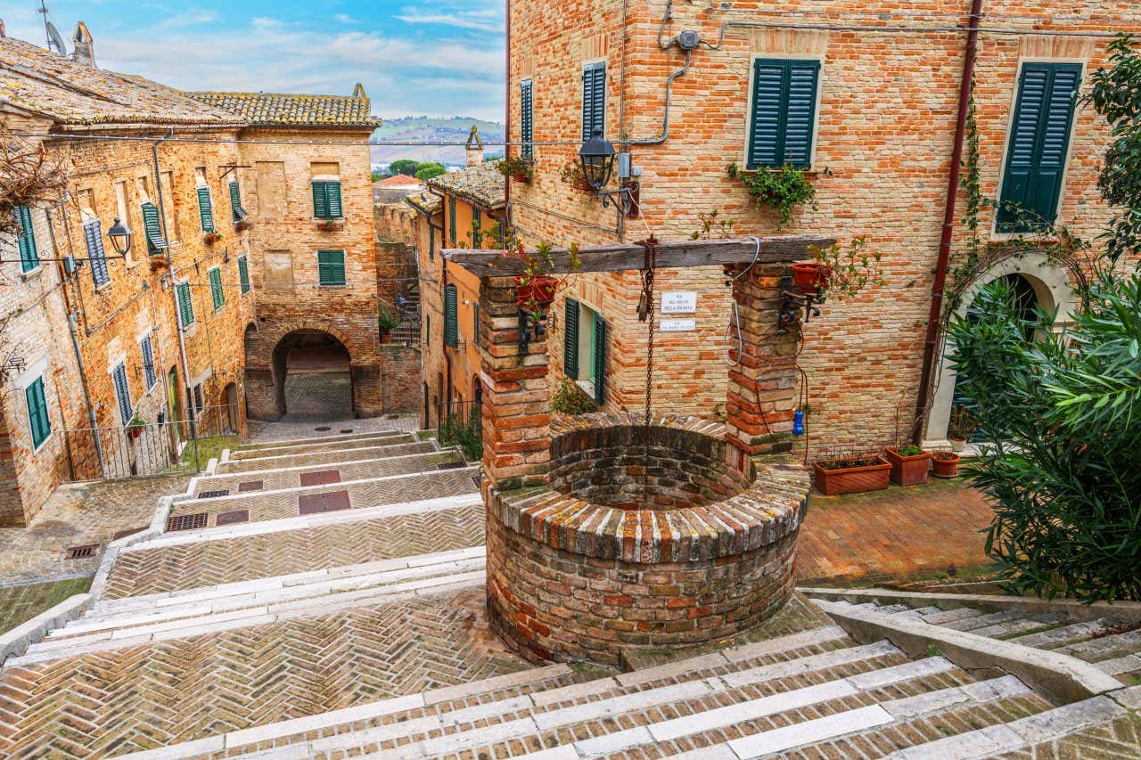 Una scalinata in mattoni circondata da bassi edifici medievali in mattoni a vista di colore giallo, a metà della scalinata, in primo piano, c'è un pozzo