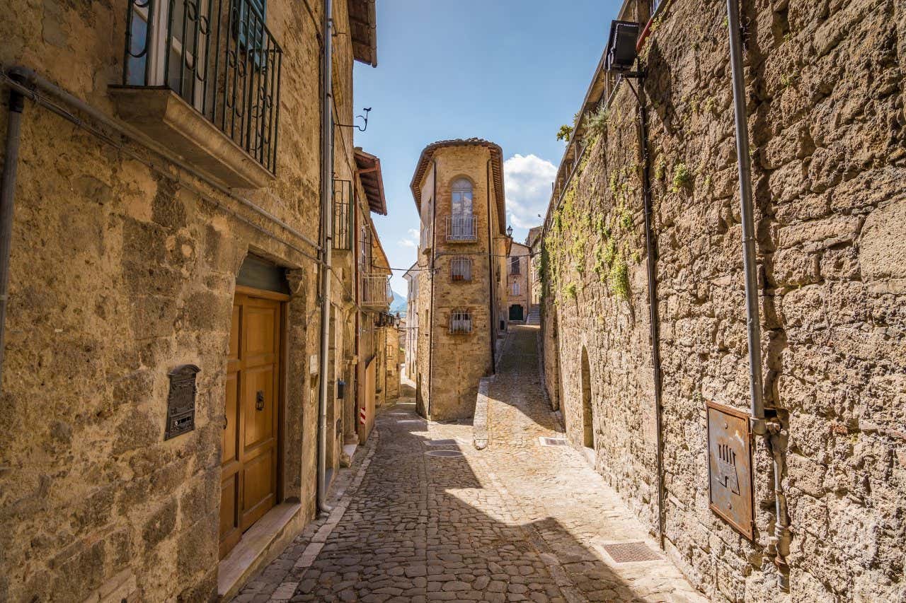 Scorcio di una stretta via acciottolata di un paese italiano, accerchiata da piccoli palazzi in pietra 