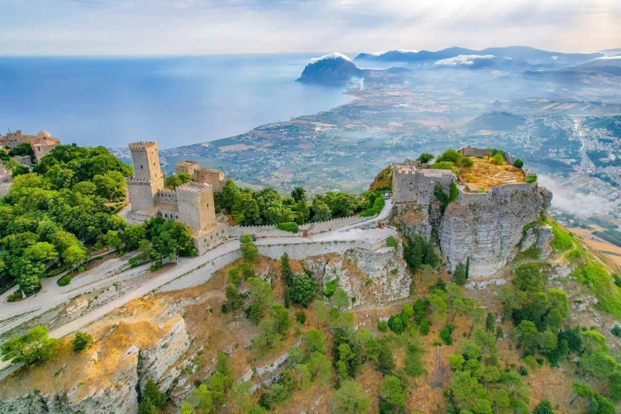 I resti di un antico castello arroccato sulla cima rocciosa di un monte e sullo sfondo la vista di campagne a centri urbani vicini al mare