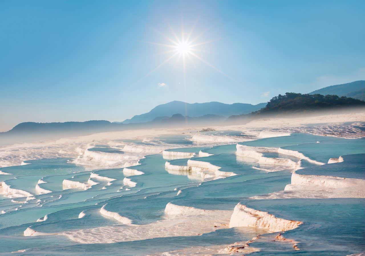 Pamukkale (The Cotton Castle) with a light haze above the ground and a clear sky with the sun in the background.