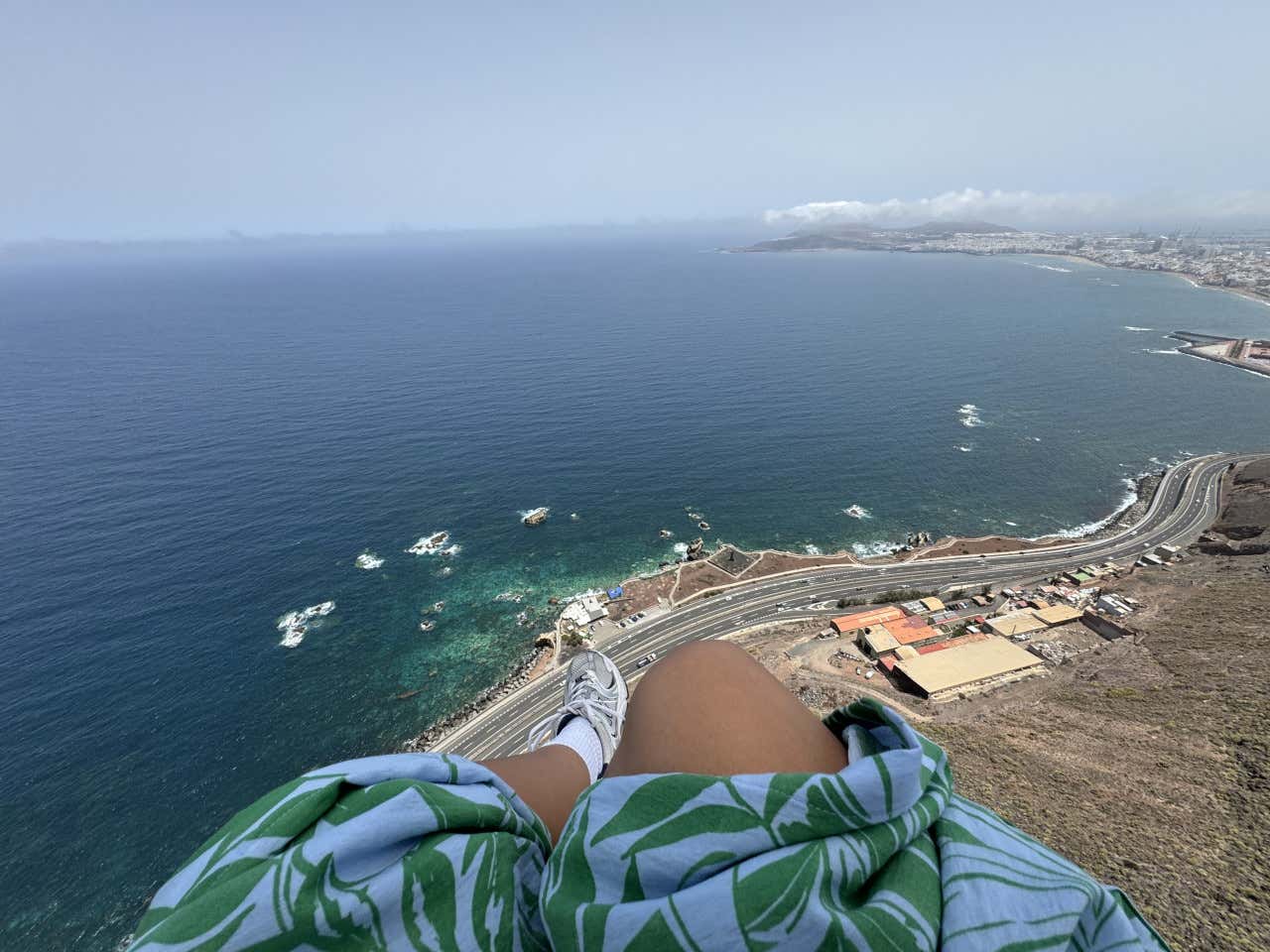 Primer plano de las piernas de una mujer con vestido volando en parapente y al fondo el mar de Gran Canaria