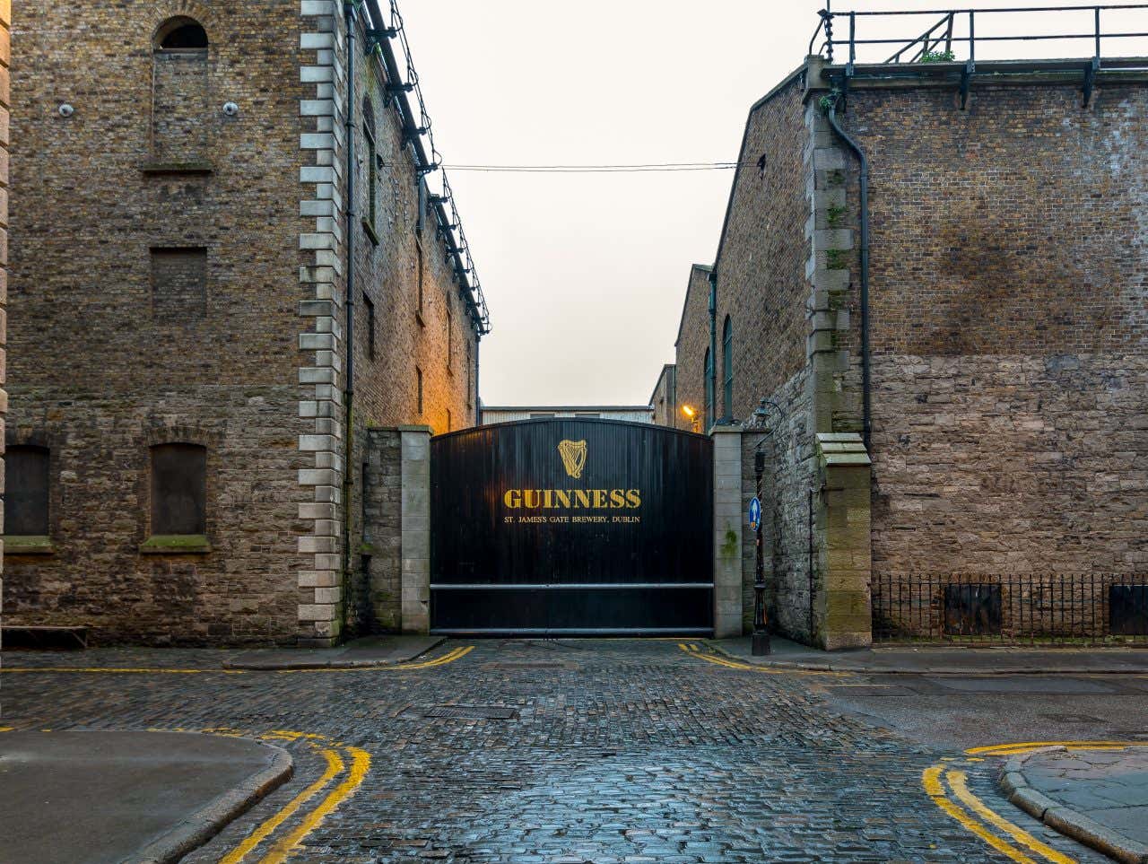 Il portone nero che funge da ingresso alla fabbrica della Guinness, con grandi edifici in mattoni ai lati e un cielo grigio sullo sfondo