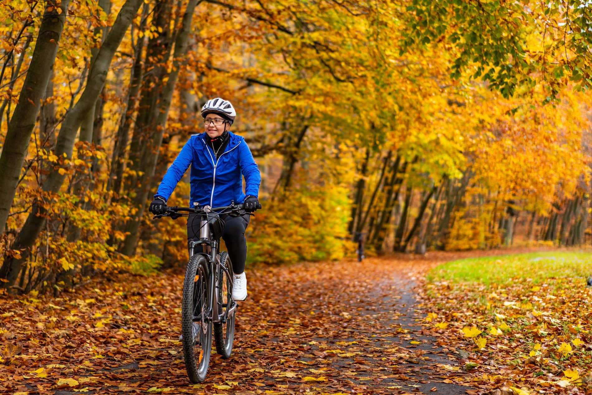 Una donna in bicicletta percorre un sentiero ricoperto di foglie arancioni vicino a degli alberi con foglie gialle. Una delle attività nella comunità di Madrid per godersi l'autunno.