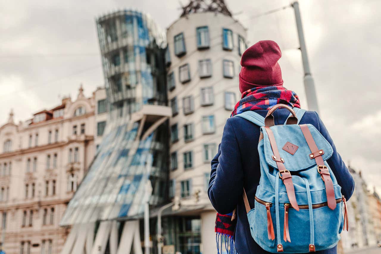 Un turista con una mochila de espaldas a la cámara contemplando la fachada moderna de la Casa Danzante de Praga