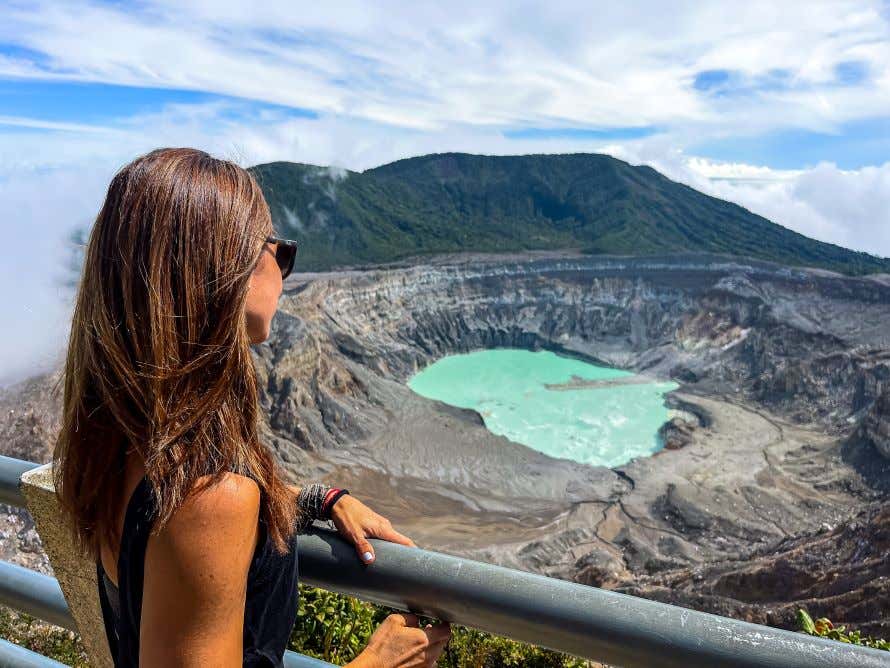 Una donna di spalle osserva la laguna sulfurea di un cratere vulcanico da un belvedere