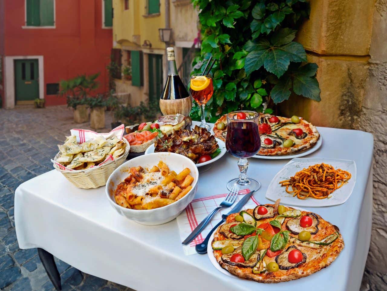 A table with various Italian dishes: pizza, macaroni, spaghetti, among others, and wine.