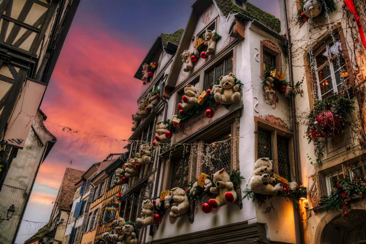 Varios osos de peluches con bolas de Navidad colgando de una casa en Estrasburgo al atardecer