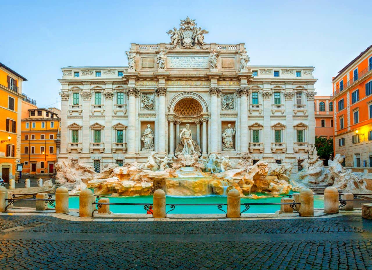 A view of the Trevi Fountain under a blue sky, with no one around it.