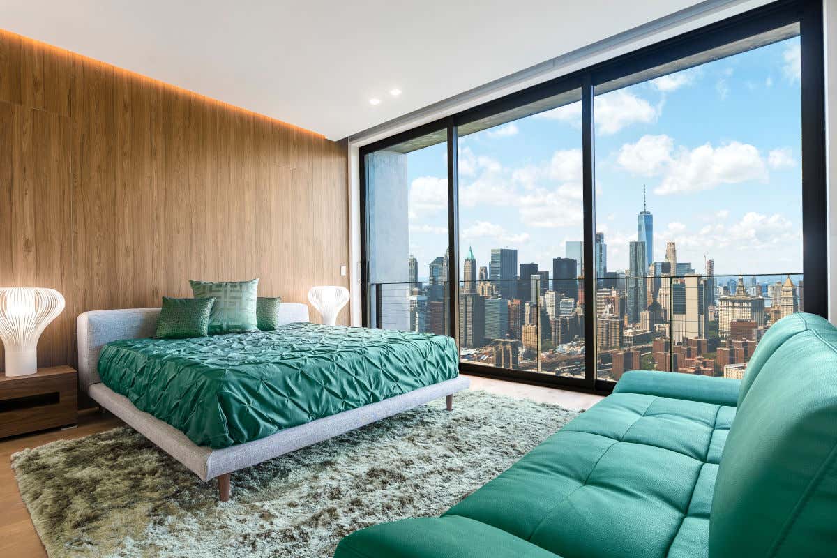 Una habitación de hotel con cama, sofá y una gran ventana con vistas a los rascacielos de Nueva York