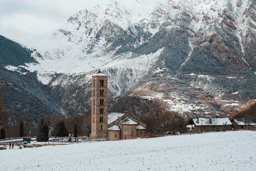 Campanario de una iglesia románica con unas montañas nevadas de fondo