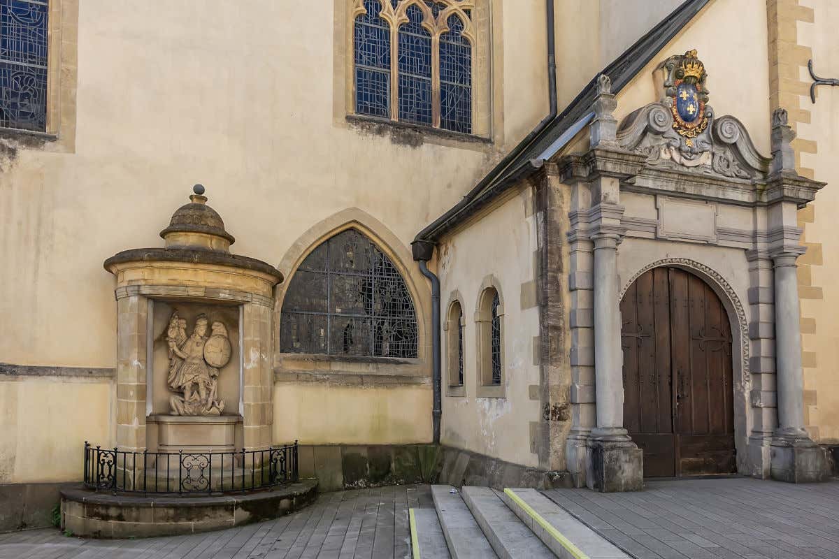 Exterior de igreja com alpendre decorado com escudo e escultura em pedra de um arcanjo