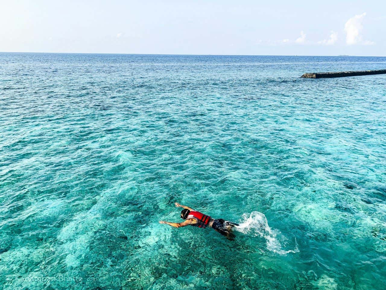 A man wearing a red lifejacket snorkelling in turquoise waters